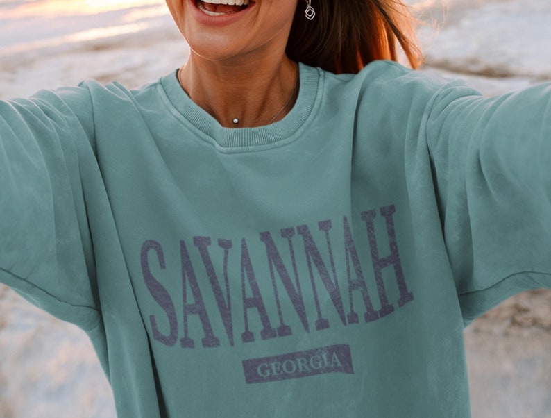 K&ouml;nnte beinhalten: Ein blaugr&uuml;ner Pullover mit dem Aufdruck "SAVANNAH GEORGIA" in dunkelblau.