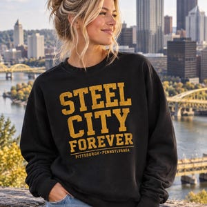 以下が含まれることがあります： 黒のクルーネックのスウェットシャツ。前面にはゴールドの文字で「STEEL CITY FOREVER」、その下に小さく「PITTSBURGH • PENNSYLVANIA」とプリントされています。グラフィックには使い古したようなかすれた質感が施されています。