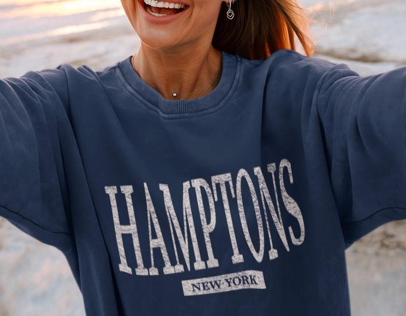 May include: A navy blue sweatshirt with the text "HAMPTONS NEW YORK" printed in white on the front.