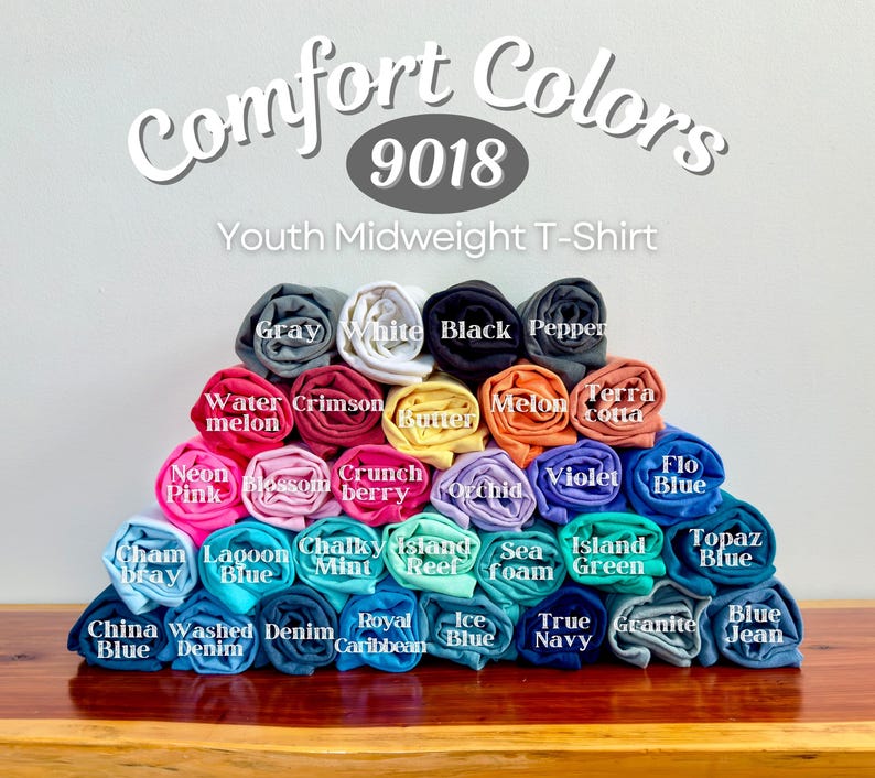 May include: A pyramid stack of rolled Comfort Colors 9018 Youth Midweight T-Shirts in various colors including gray, white, black, pepper, watermelon, crimson, butter, melon, terracotta, neon pink, blossom, crunchberry, orchid, violet, flo blue, chambray, lagoon blue, chalky mint, island reef, seafoam, island green, topaz blue, china blue, washed denim, denim, royal caribbean, ice blue, true navy, granite, and blue jean.