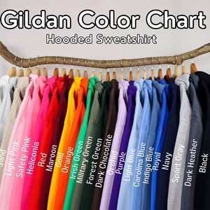 Puede incluir: Una carta de colores Gildan para sudaderas con capucha que muestra una fila de sudaderas de varios colores colgadas de una rama de madera. El texto dice Gildan Color Chart Hooded Sweatshirt, con etiquetas para cada color, incluyendo White, Ash, Sand, Light Pink, Safety Pink, Heliconia, Red, Maroon, Gold, Orange, Irish Green, Military Green, Forest Green, Dark Chocolate, Orchid, Purple, Light Blue, Carolina Blue, Indigo Blue, Royal, Navy, Sport Gray, Dark Heather y Black.