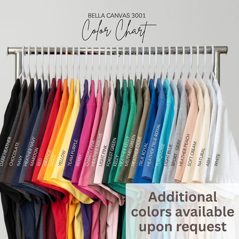 May include: A Bella Canvas 3001 color chart displaying a row of t-shirts on white hangers. The shirts are arranged in a spectrum of colors including black, dark heather, chocolate, navy, maroon, red, orange, gold, yellow, purple, berry, pink, green, blue, gray, peach, cream, and white, with text labels for each color.