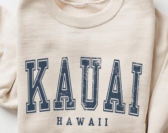 Könnte beinhalten: Ein beiger Pullover mit einem marineblauen Vintage-Grafikdruck, der "KAUAI HAWAII" lautet.