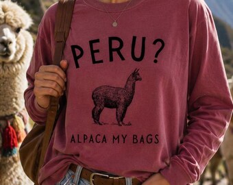 Puede incluir: Una sudadera de manga larga con cuello redondo en un color rosa polvoriento apagado. El frente presenta el texto negro PERU? sobre una ilustración de línea negra de una alpaca, con el texto ALPACA MY BAGS impreso en negro debajo.
