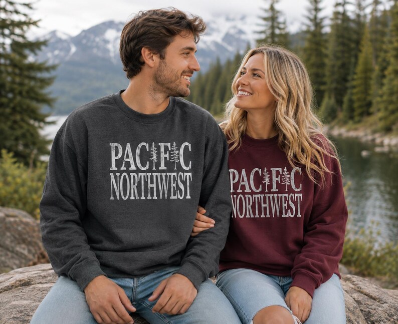 May include: A dark charcoal gray crewneck sweatshirt and a maroon crewneck sweatshirt, both featuring the white distressed text PACIFIC NORTHWEST with a pine tree graphic replacing the letter I in the word PACIFIC on the front of each garment.