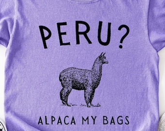 Puede incluir: Una camiseta de manga corta de color morado claro con un gráfico negro de una alpaca en el centro. Encima de la alpaca aparece el texto PERU? y debajo el texto ALPACA MY BAGS. La camiseta tiene una etiqueta de la marca Comfort Colors.