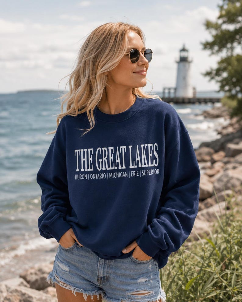 May include: A navy blue crewneck sweatshirt featuring the white text THE GREAT LAKES followed by the names HURON | ONTARIO | MICHIGAN | ERIE | SUPERIOR printed in a clean, sans-serif font across the chest area of the long-sleeved garment.