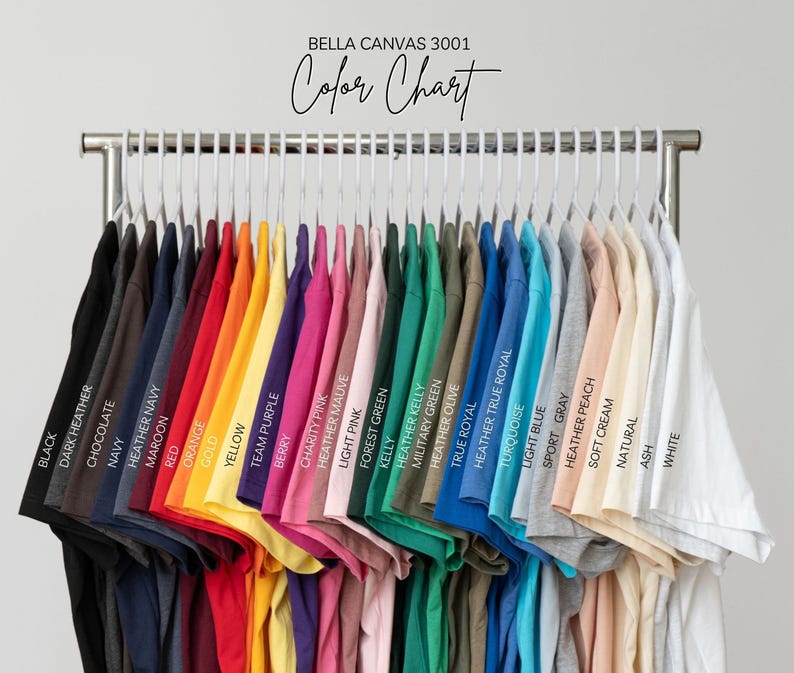 May include: A color chart of Bella Canvas 3001 t-shirts, displayed on a clothing rack. The shirts are in various colors, including black, navy, red, yellow, pink, green, blue, and white. The text "Color Chart" is above the shirts.