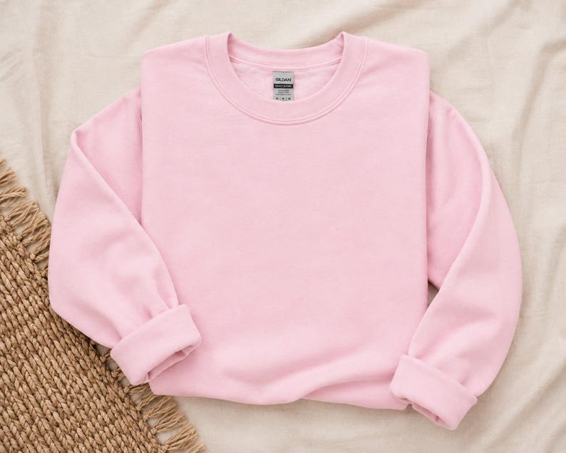 Pode incluir: Uma camisola de manga comprida e gola redonda num tom rosa claro s&oacute;lido, com punhos e bainha canelados. A pe&ccedil;a apresenta uma etiqueta da marca Gildan no interior da gola. A camisola &eacute; simples, sem quaisquer desenhos gr&aacute;ficos ou padr&otilde;es.