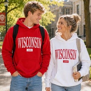 Puede incluir: Una sudadera con capucha roja con el texto WISCONSIN y 1848 en blanco, y una sudadera con capucha blanca con el texto WISCONSIN y 1848 en rojo. Ambas prendas cuentan con un bolsillo tipo canguro, mangas largas y una capucha con cord&oacute;n.