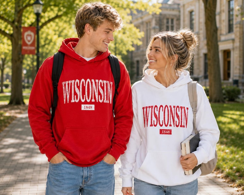 Puede incluir: Una sudadera con capucha roja con el texto WISCONSIN y 1848 en blanco, y una sudadera con capucha blanca con el texto WISCONSIN y 1848 en rojo. Ambas prendas cuentan con un bolsillo tipo canguro, mangas largas y una capucha con cord&oacute;n.