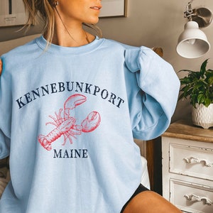 May include: Light blue sweatshirt with a red lobster graphic and the text "KENNEBUNKPORT MAINE" in navy blue.