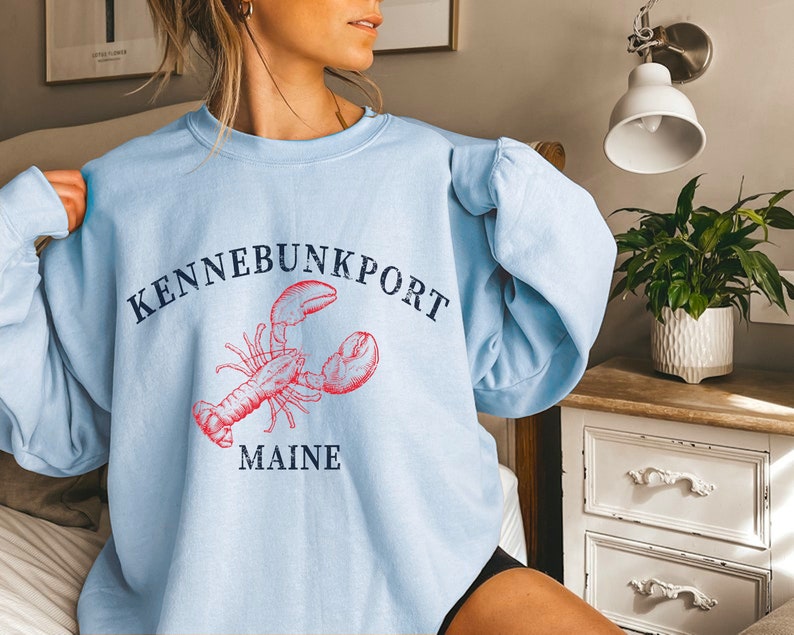May include: Light blue sweatshirt with a red lobster graphic and the text "KENNEBUNKPORT MAINE" in navy blue.