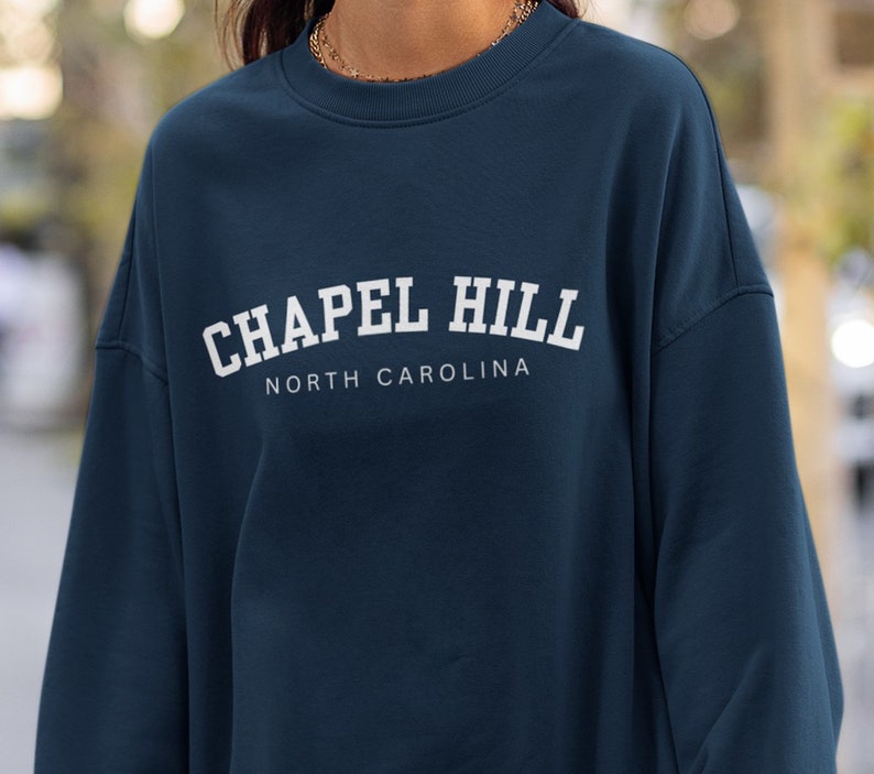 Puede incluir: Una sudadera azul oscuro con texto blanco que dice "Chapel Hill North Carolina".