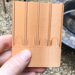 May include: A 3D printed orange plastic card holder with five slots. The card holder has a textured surface and a slightly curved design.