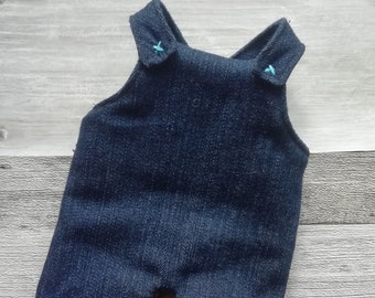 Puede incluir: Un mono vaquero con costuras azules. El mono tiene un estilo de babero con dos tirantes que se cruzan en la espalda.