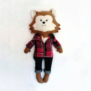 May include: A brown werewolf plush toy wearing a red and black plaid shirt and blue jeans. The toy has a white face with black eyes and a black nose.