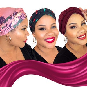 May include: Three women wearing head wraps in different colors and patterns. One wrap is pink with a floral design, another is black with red and green accents, and the third is a braided burgundy style. All women are wearing hoop earrings and red lipstick.