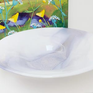 May include: A white ceramic bowl with a slightly rippled surface. The bowl has a subtle iridescent sheen and is perfect for serving snacks or fruit.