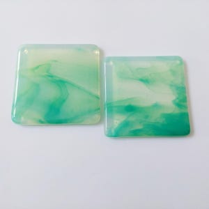 May include: Two square green and white glass coasters with a marbled design.
