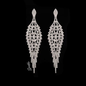 May include: A pair of long, silver dangle earrings with a geometric design made of clear rhinestones. The earrings are very sparkly and would be perfect for a special occasion.