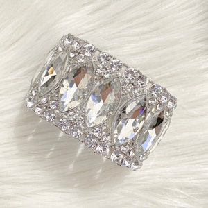 May include: A silver bracelet with a row of large, clear, faceted crystals surrounded by smaller crystals.
