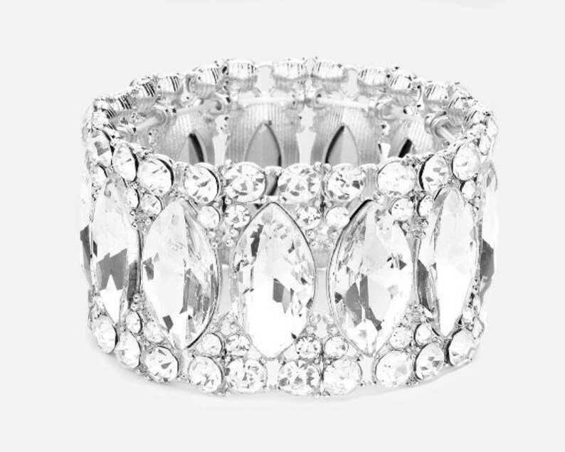 May include: A silver bracelet with a row of large, clear, faceted crystals. The crystals are set in a silver band and are arranged in a staggered pattern.
