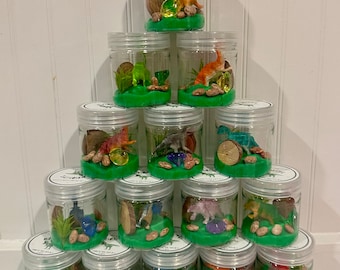 May include: A set of 18 clear plastic jars filled with green play dough, small plastic dinosaurs, and other small objects. The jars are arranged in a pyramid shape.