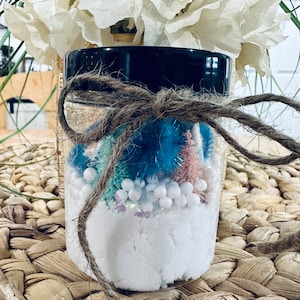 May include: A clear glass jar filled with white powder, white beads, and colorful pipe cleaners. The jar is tied with brown twine and has a black lid.