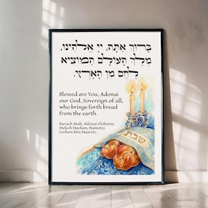 May include: A framed print featuring Hebrew text and English translation. The artwork includes an illustration of challah bread, candles, and a blue tablecloth. The print is in a black frame and is displayed against a white wall.