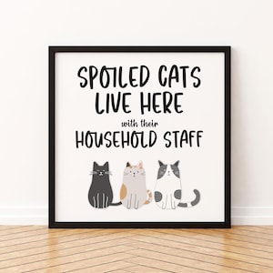 May include: A black framed print with white background and black text that reads "Spoiled Cats Live Here with their Household Staff". Three cartoon cats are pictured below the text: a black cat, a calico cat, and a gray and white cat.