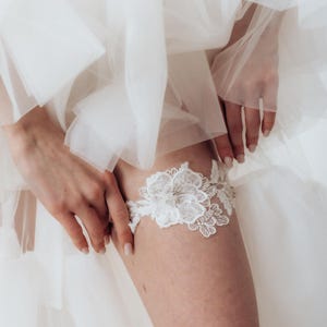 May include: White lace garter with a floral design and a pearl embellishment.