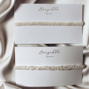 A collection of delicate bridal accessories is displayed on elegant white cards. The accessories include a lace garter, a floral chiffon garter, and a pearl-embellished garter, all in soft ivory tones. The presentation exudes a romantic and sophisticated bridal aesthetic.
