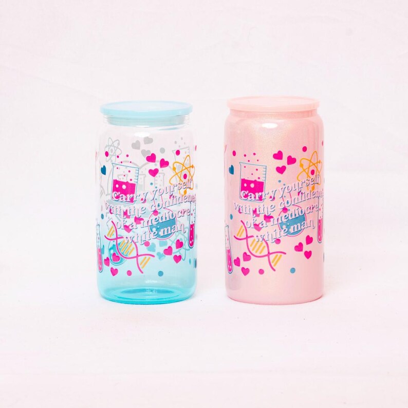 May include: Two glass tumblers with lids, one blue and one pink, are displayed. Each tumbler features a science-themed design with hearts, beakers, and the text "Carry yourself with the confidence of a mediocre white man."