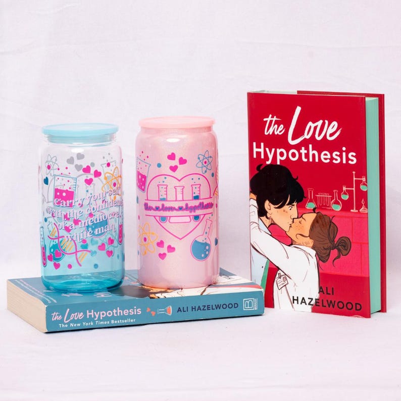 May include: Two glass tumblers with lids, one blue and one pink, are decorated with hearts and science-themed graphics. A hardcover book titled "The Love Hypothesis" is also visible, along with a second book with the same title. The image has a white background.