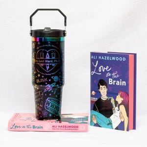 Puede incluir: Un vaso térmico negro con asa, con un diseño colorido con texto e ilustraciones. El vaso está junto a dos ejemplares del libro "Love on the Brain" de Ali Hazelwood.