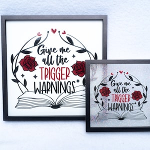 May include: Two framed prints with a black frame and a white background. The print features a black and white illustration of an open book with red roses and vines. The text on the print reads "Give me all the trigger warnings".