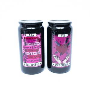 May include: Two black glass jars with pink and black labels. The jar on the left has the text "XXX" and "THE TROPES" on the label. The jar on the right has the text "VIII" and "WHY CHOOSE" on the label.