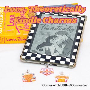 Puede incluir: Un lector de libros electrónicos Kindle con una funda a cuadros en blanco y negro muestra una ilustración de la portada de un libro. Tres colgantes acrílicos con texto e ilustraciones cuelgan debajo. El texto "Love, Theoretically" es visible en el lector y un libro.