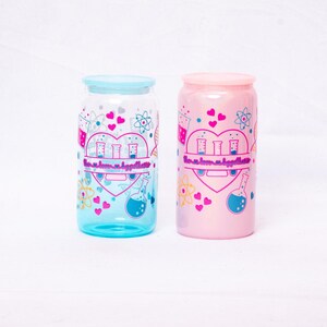 May include: Two glass can-shaped tumblers, one blue and one pink, with matching lids. Each tumbler features a heart-shaped design with science-themed graphics, including beakers, atoms, and the text "love, science, hypothesis".