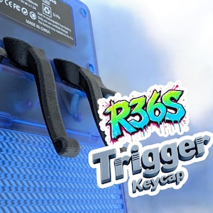 May include: Black trigger keycaps for the R36S handheld gaming device. The keycaps are positioned over a blue, textured surface. The image also includes the text "R36S Trigger Keycap" in a graffiti-style font.