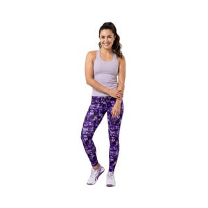 May include: A woman wearing a light purple tank top and purple floral leggings. The leggings have a dark purple background with a pattern of lighter purple flowers. She is wearing white athletic shoes.