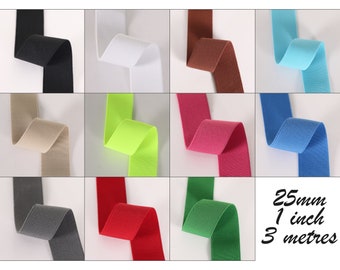 Op de afbeelding: Een selectie van 1 inch brede elastiek in verschillende kleuren, waaronder zwart, wit, bruin, lichtblauw, beige, limoengroen, roze, blauw, grijs en rood. Het elastiek is 3 meter lang.