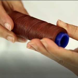 Może przedstawiać: Szpula brązowej nici woskowanej z niebieskim plastikowym zakończeniem.