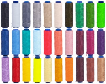 Op de afbeelding: Een verzameling van 24 spoelen gewaxt garen in verschillende kleuren, waaronder zwart, wit, blauw, groen, rood, roze, paars, geel, oranje en bruin. De spoelen zijn gerangschikt in twee rijen van 12.