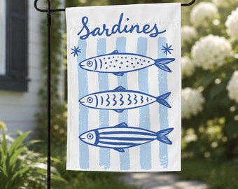 May include: A white garden flag featuring the word Sardines in blue script at the top. Below the text are three stylized blue fish illustrations arranged vertically over a background of light blue vertical stripes and two small blue star icons.
