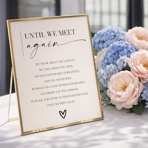 May include: A framed sign with the text "UNTIL WE MEET again" in elegant script. The sign includes a heartfelt poem and a heart symbol. A bouquet of blue and pink flowers sits beside the sign, creating a soft, comforting atmosphere.
