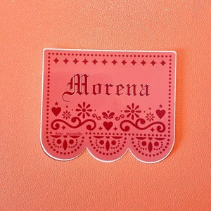May include: A pink paper banner with a scalloped edge and red decorative details. The banner says "Morena" in a stylized font.