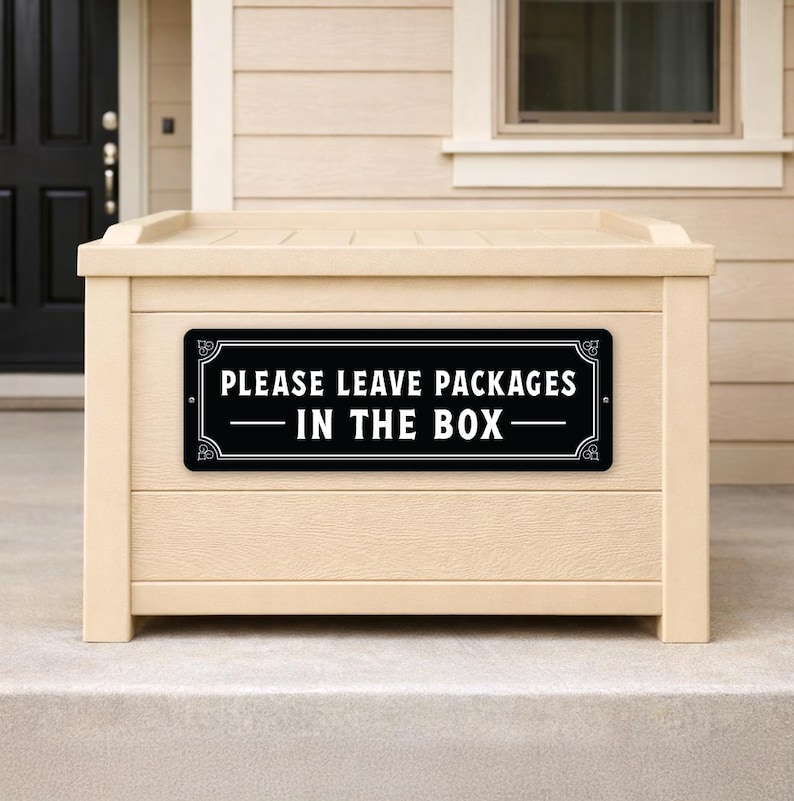 May include: A beige package drop box with a black and white sign that reads "PLEASE LEAVE PACKAGES IN THE BOX". The box is made of wood and has a flat top. The sign is rectangular with decorative corners.
