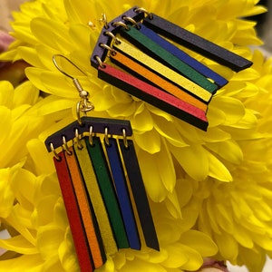 May include: A pair of rainbow-colored wooden earrings with a dangling design. The earrings are made of multiple thin strips of wood in red, orange, yellow, green, blue, and purple. The strips are attached to a small metal ring at the top.